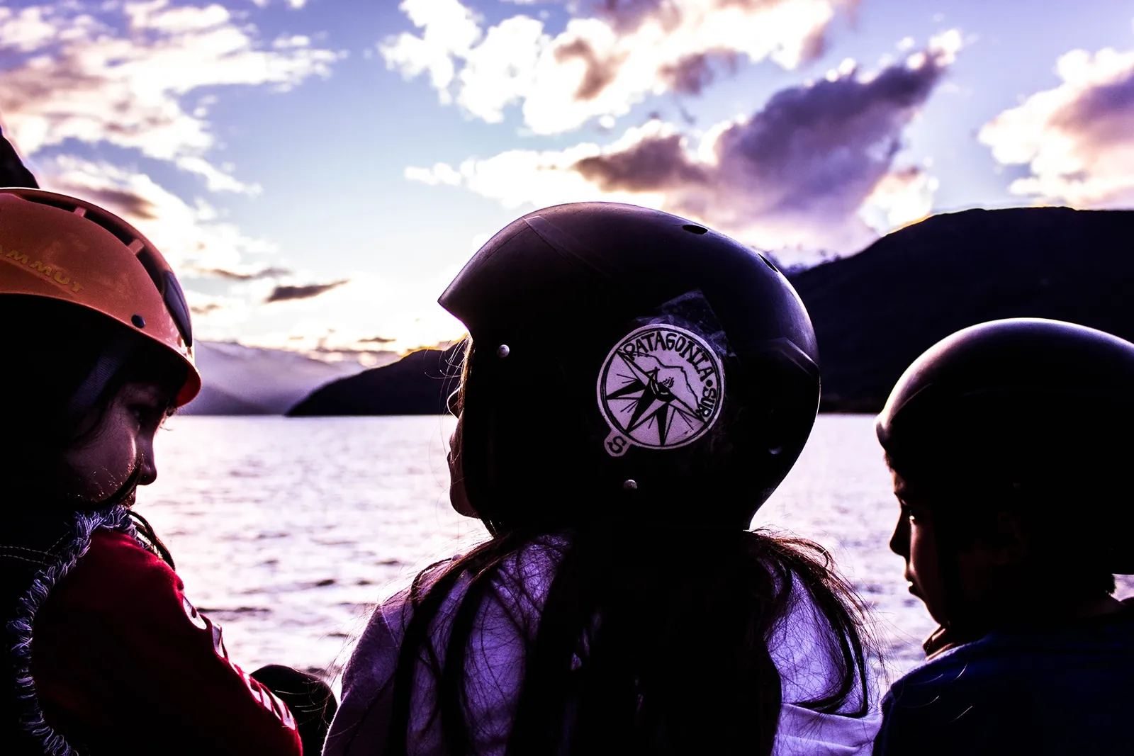 Viajeros de Patagonia Punto Sur con casco y el símbolo de la marca, frente a un lago